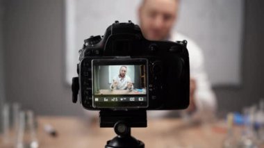 Evdeki video stüdyosunda online kimya öğretmeni kayıtları var. Beyaz önlüklü, sakallı, beyaz bir adam keçeli kalem tahtasının arkasında oturuyor. Molekülün modelini gösterir.