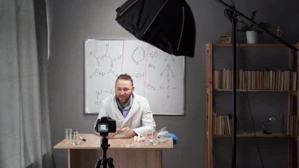 在线导师化学老师记录Vlog在家里的家庭视频工作室 一个身穿白衣 留着胡子的高加索人坐在一块标牌的后面 — 图库视频影像