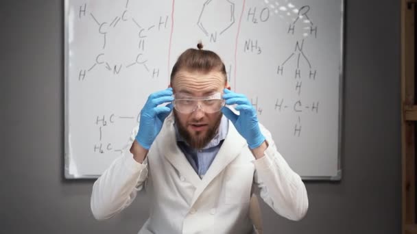 在线导师化学老师记录Vlog在家里的家庭视频工作室 一个留着胡子的白衣男子坐在一块白板的后面 戴防护护目镜 — 图库视频影像