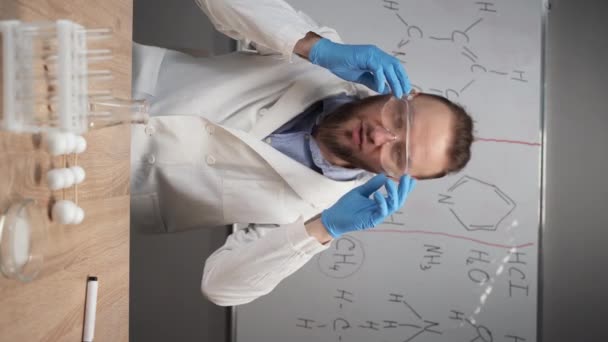 化学教师或导师坐在一个带有化学配方的标记板的背景下 戴上护目镜准备实验 垂直录像 视频会议摄像头肖像 — 图库视频影像