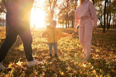 Aile: baba, anne ve oğul güneş batarken sonbahar parkında oynuyorlar. Boşluğu kopyala