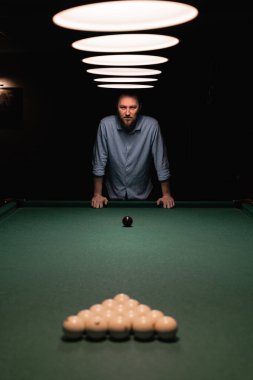 Sakallı beyaz bir adam bilardo masasının yanında duruyor ve oyuna hazırlanıyor. Bilardo sporu konsepti. Boşluğu kopyala.