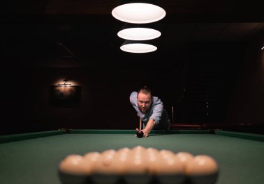 Sakallı beyaz bir adam bilardo masasının yanında duruyor, oyunun başlamasına hazırlanıyor, eğiliyor, elinde bir ıstaka tutuyor, nişan alıyor. Bilardo sporu konsepti. Boşluğu kopyala.