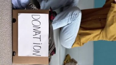 Donut metniyle karton bir kutunun yakın çekimi. Kadınların elleri kıyafet katlar. Bir kadın kıyafet bağışlıyor. Yaşam tarzı, sürdürülebilir kavram. dikey video.
