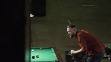 Beyaz adam bilardo oynuyor ve barda bira içiyor. Bilardo oyununun bir parçası devam ediyor. Bilardo sporu konsepti. Boşluğu kopyala
