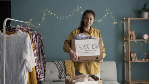 家里有捐款箱的快乐女人女性手中有衣服的穷人捐赠盒 微笑的女人拿着一盒捐赠的衣服 复制空间 — 图库视频影像
