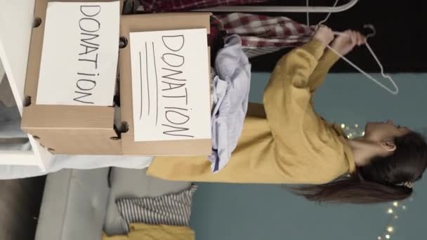 服の寄付のための段ボール箱を準備する女性 寄付する前に家で服を準備する 寄付の概念 垂直ビデオ — ストック動画