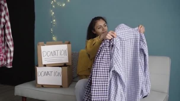 家で貧しい人のために古い服を準備する女性 寄付ラベルと布の梱包箱 服寄付の考え方 — ストック動画