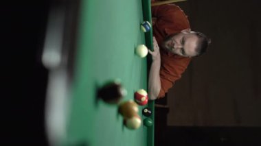 Bilardo kulübünde bilardo oynayan ciddi bir adam bilardo topuna vuruyor. Dikey video