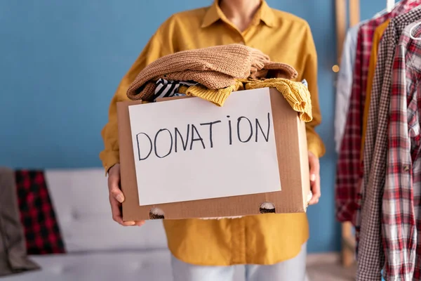 Donation concept. Woman holding Donation box with donation clothes in her home. Charity. Helping poor people. Close-up