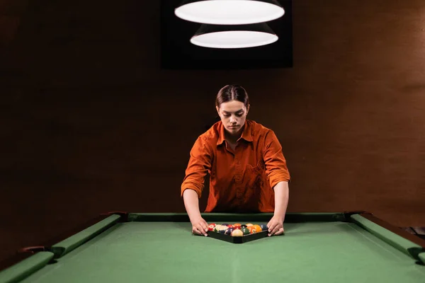 Sports game of billiards on a green cloth. Caucasian woman collect multi colored billiard balls in the form of a triangle with numbers shoot. Sports games, outdoor activities. Copy space