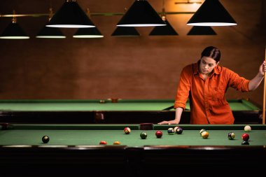 Amerikan bilardosu oynayan güzel genç kız bilardo masasını düşünüyor. Bilardo sporu konsepti. Boşluğu kopyala