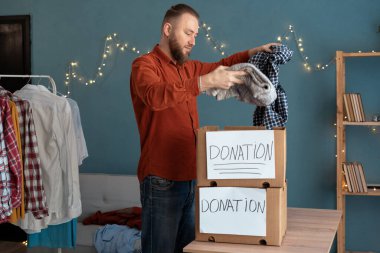 İlgili erkek gönüllü, ihtiyaç sahiplerine bağış kutusuna giysi koydu. İnsan giysilerini pakete koyup fakirlere bağışlıyor. Geri dönüşüm ve yardım konsepti. Boşluğu kopyala