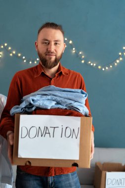 Fakir ve muhtaç insanlar için kullanılmış giysilerle dolu bağış kutusuyla gülümseyen adamın portresi. Bağış ve yardım konsepti.