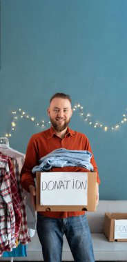 Fakir ve muhtaç insanlar için kullanılmış giysilerle dolu bağış kutusuyla gülümseyen adam. Bağış ve yardım konsepti.