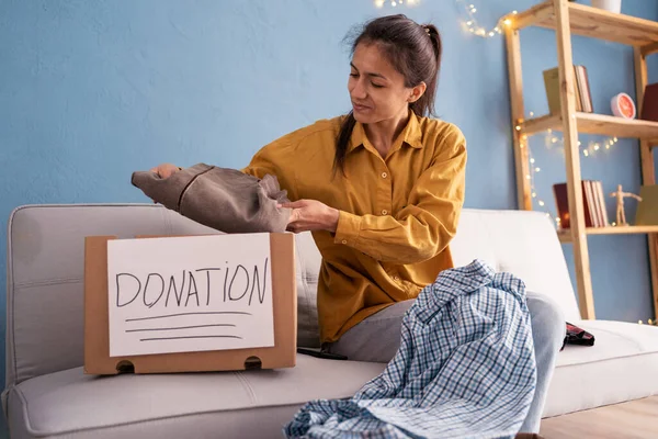 Bağış konsepti. Eski kıyafetlerini evde bir bağış kutusuna dizip hazırlayan bir kadın. Boşluğu kopyala