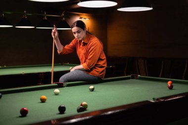 Düşünceli kız bilardo oynar. Arka planda bilardo odası var. Boşluğu kopyala