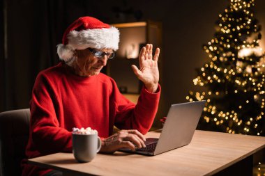 Çevrimiçi iletişim ve akrabalarla iletişimde kalmak. Noel 'de Noel Baba şapkalı büyükbaba evde oturuyor, ailelerini arıyor ve torunlarına el sallıyor. Boşluğu kopyala
