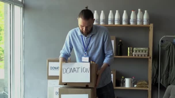 男性ボランティアは 配布または難民支援センターの箱から食べ物を梱包解除します チャリティー ボランティアのコンセプト — ストック動画
