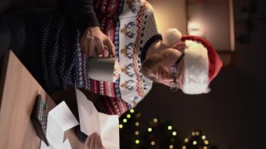 Ofis masasında oturan adam fatura bilgilerini ya da arka planda Noel ağacı olan bir mektubu okuyarak fazla mesai yapıyor. Dikey video