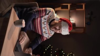 Genç ve mutlu bir adam, evde tek başına Noel 'i kutlarken bilgisayarını açıp elini sallıyor ve arkadaşlarıyla iletişim kuruyor. Dikey video
