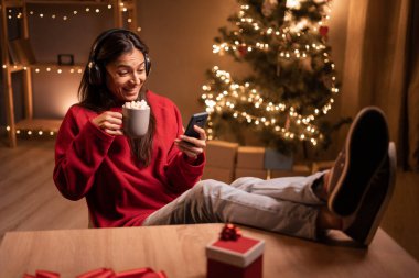 Kulaklıklı, müzik dinleyen ya da Noel arifesinde evde film izleyen mutlu genç bir kadın. Boşluğu kopyala