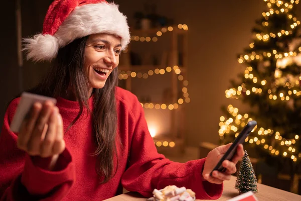 Noel Baba şapkası takan kadınlar, ellerinde kredi kartı ve ev telefonlarıyla Noel tatili boyunca ev telefonlarını kullanıyorlar. Noel alışverişi konsepti. Boşluğu kopyala