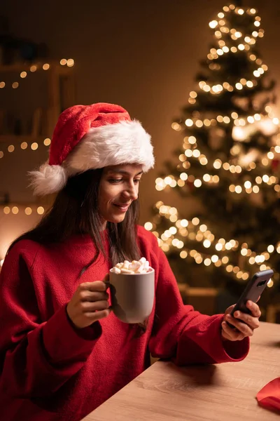 Pozitif genç bir kadının portresi evde cep telefonu tutacağı bardağı ve yılbaşı süslemeleri kullanıyor. Boşluğu kopyala