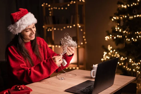 İnternetten Noel alışverişi yapan genç bir kadın ev ya da küçük ofis dekorasyonu için çelenk açıyor. Boşluğu kopyala