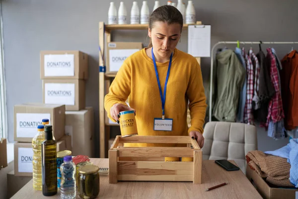 Dağıtımda ya da mülteci yardım merkezinde yoksullar için bir kutu yiyecek paketleyen gönüllü bir kadın. Bağış konsepti. Boşluğu kopyala