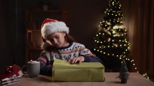 十代の女の子はクリスマスのイブのテーブルの家に坐っている間ペーパーでクリスマスのギフトを包んでいる 死と冬の休暇の概念 — ストック動画