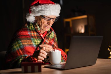 Yaşlı adam modern cihazla noel filmi izliyor, evde kakao içiyor. Boşluğu kopyala
