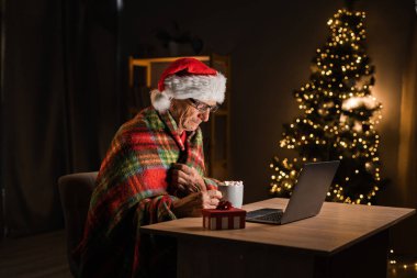 Yaşlı adam Noel 'de evde kakao içiyor ve bilgisayar ekranına bakıyor. Boşluğu kopyala