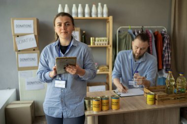 Yardım merkezinde çalışan beyaz gönüllü bir çift. Tablet tutan mutlu bir kadın. Boşluğu kopyala