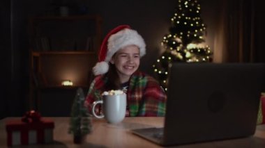 Neşeli bir kız çocuğu marshmallow yerken güler ve evde yalnız başına dizüstü bilgisayardan noel komedi filmi izler. Boşluğu kopyala