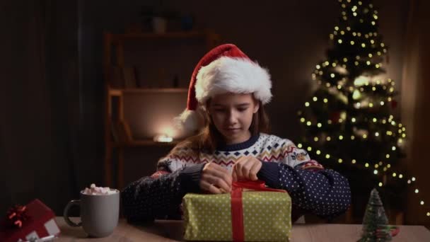 Cute Dziewczynka Siedzi Przy Stole Salonie Dekoracji Świątecznych Rozpakować Prezent — Wideo stockowe
