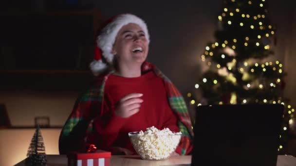 팝콘을 기분좋은 소녀가 웃으며 저녁에 집에서 컴퓨터로 크리스마스 코미디 영화를 — 비디오