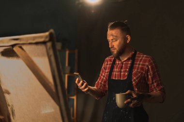 Karanlık yaratıcı stüdyodaki yetenekli erkek sanatçı yağlı boya tablonun modern başyapıtını yarattı, resim çiziyor. Şövaledeki büyük tuval. Boşluğu kopyala