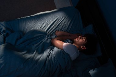 Geceleri yatak odasında rahat bir yatakta uyuyan genç adamın en iyi görüntüsü. Gece mavisi renkler ve pencereden yansıyan ışık. Millet, rahatlayın ve rahatlayın.