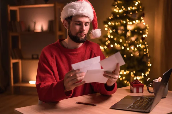 サンタの帽子をかぶっている男はクリスマスの間に封筒に請求書と手紙を持っている スペースのコピー — ストック写真