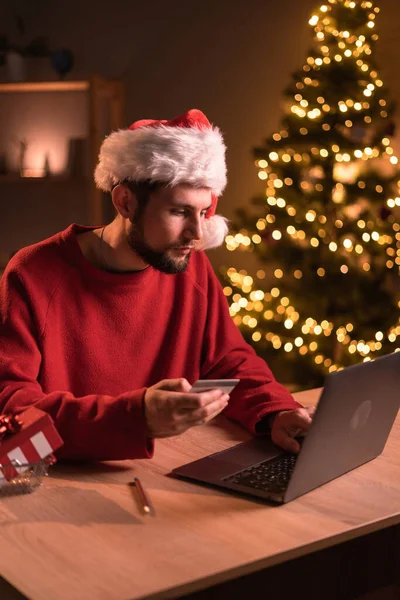 Zakupy Online Podczas Wakacji Człowiek Kapeluszu Mikołaja Pomocą Laptopa Karty — Zdjęcie stockowe