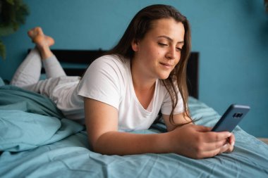 Evde rahat genç bir kadın bir mesaj okuyor ya da parlak yatak odasında arkadaşlarıyla sohbet ediyor. Boşluğu kopyala