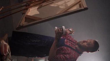 Boya fırçası kullanan erkek sanatçı akrilik tabloyu yaratıyor. Geniş tuvalli yaratıcı stüdyo. Dikey video