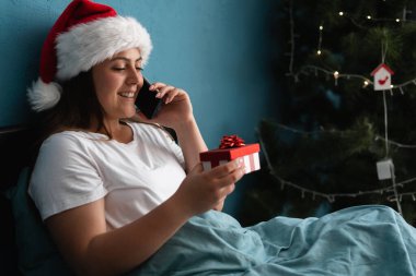 Mutlu genç bir kadın telefonda konuşuyor ve Noel 'de evde hediyesini tutuyor. Boşluğu kopyala