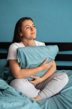 Sabahları mavi yastığa sarılan genç bir kadın rahat bir yatakta oturuyor. Boşluğu kopyala