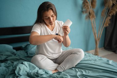 Genç bir kadın yatağında otururken nemlendirici el losyonu sürüyor.