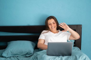 Yatakta oturan genç bir kadın, dizüstü bilgisayarında video görüşmesi yapıyor. Mutlu kız dizüstü bilgisayar ekranına el sallıyor, arkadaşlarıyla ya da aileleriyle konuşuyor. Boşluğu kopyala