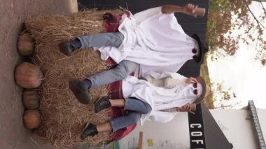 Samanlıkta oturan iki hayalet. Cadılar Bayramı partisi. Park, cadılar bayramı ve hayalet kostümlü arkadaşlar. Dikey video