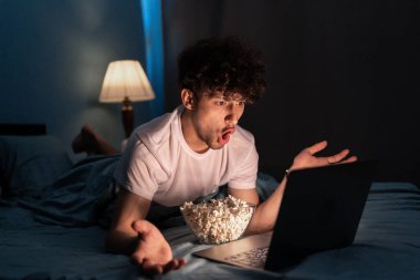 Patlamış mısır yiyen ve geceleri yatakta yatarken dizüstü bilgisayarda korku filmi izleyen harika bir adam. Boşluğu kopyala