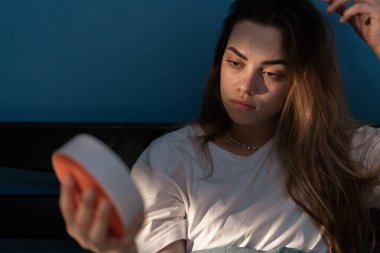 Depresyonda olan genç bir kadın yatakta oturup saate bakarken uyuyamıyor, uykusuzluk çekiyor. Uyku apnesi, uykusuzluk ya da stres konsepti. Boşluğu kopyala